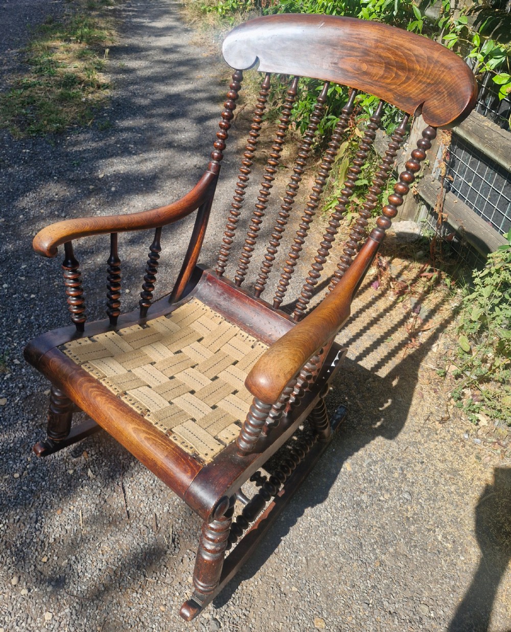 A nineteenth-century dark wood rocking chair featuring bobbin-turned spindles, curved armrests, and a woven webbing seat base.