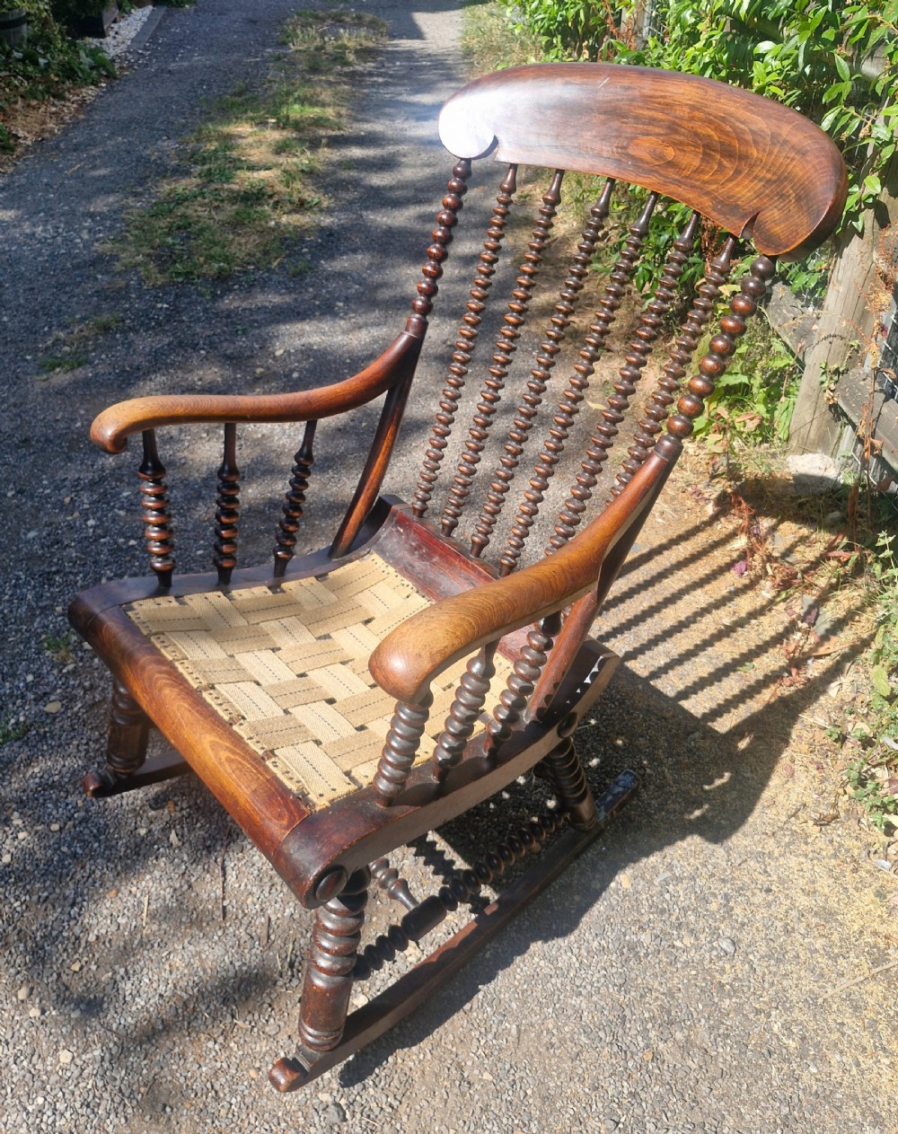 A nineteenth-century dark wood rocking chair featuring bobbin-turned spindles, curved armrests, and a woven webbing seat base. View II