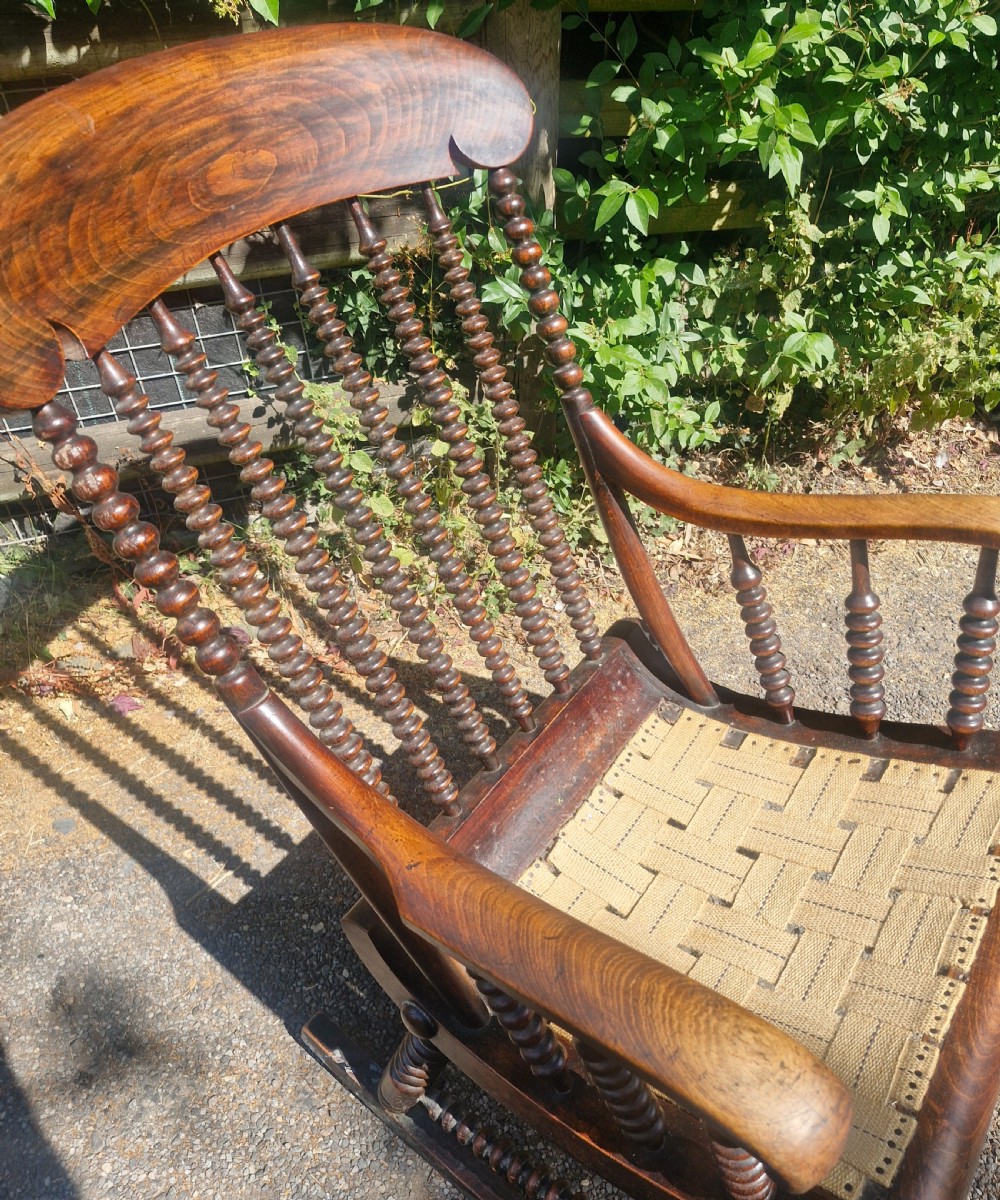 A nineteenth-century dark wood rocking chair featuring bobbin-turned spindles, curved armrests, and a woven webbing seat base. View IV