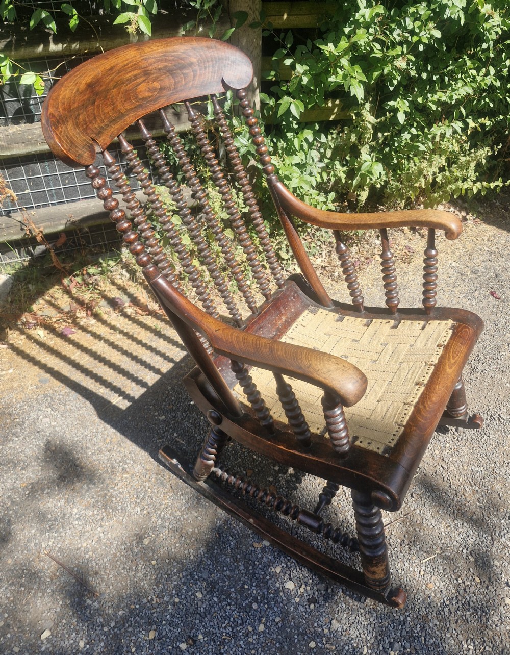 A nineteenth-century dark wood rocking chair featuring bobbin-turned spindles, curved armrests, and a woven webbing seat base. View V