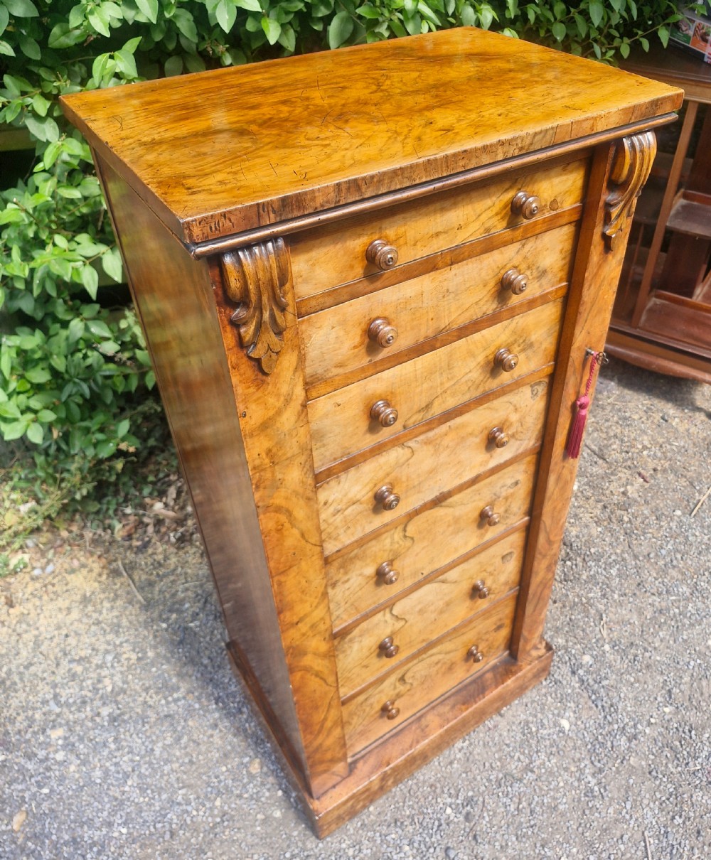 A tall Victorian walnut Wellington chest featuring seven stacked drawers with turned wooden knobs, carved upper corbels, and a side locking pilaster bar.
