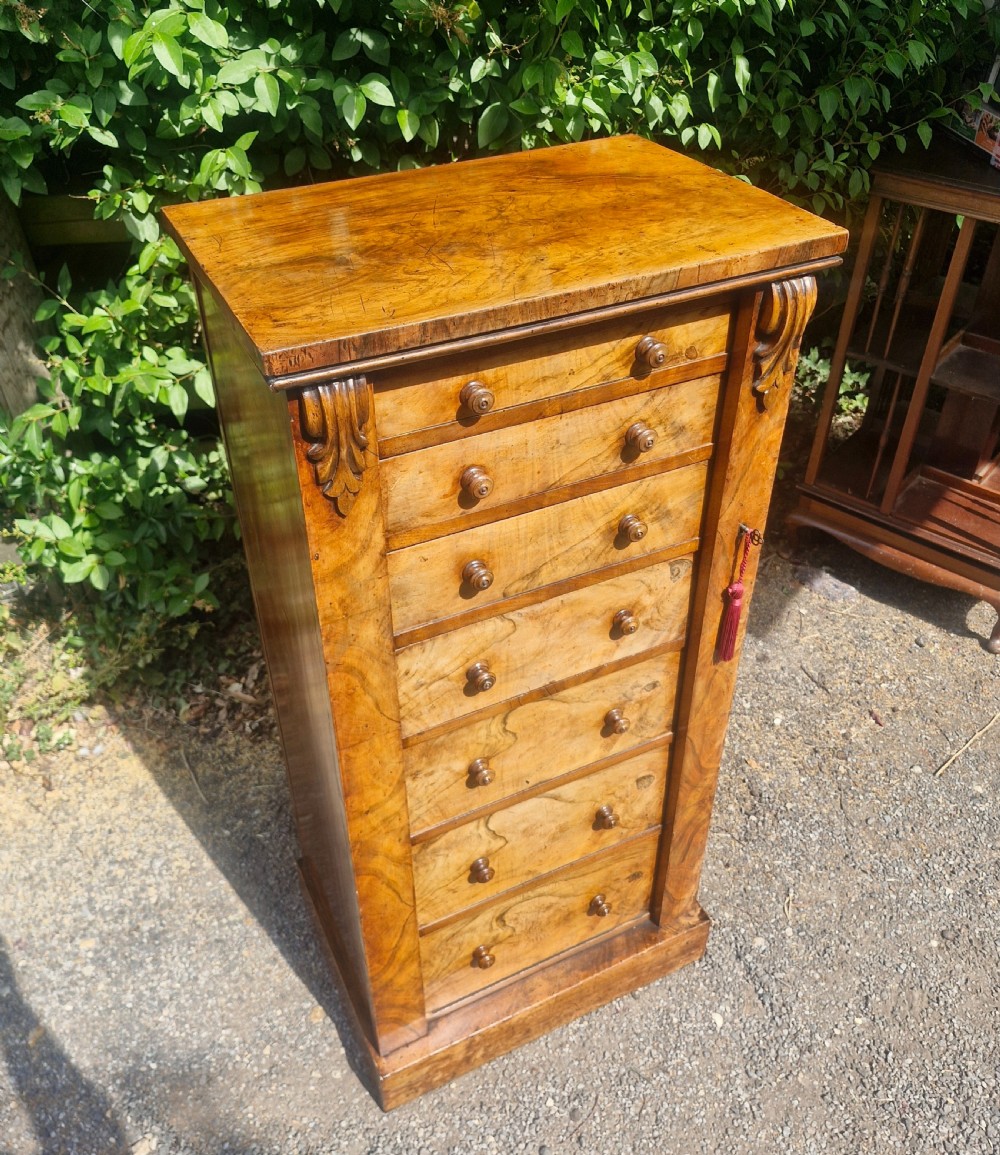 A tall Victorian walnut Wellington chest featuring seven stacked drawers with turned wooden knobs, carved upper corbels, and a side locking pilaster bar. View VI