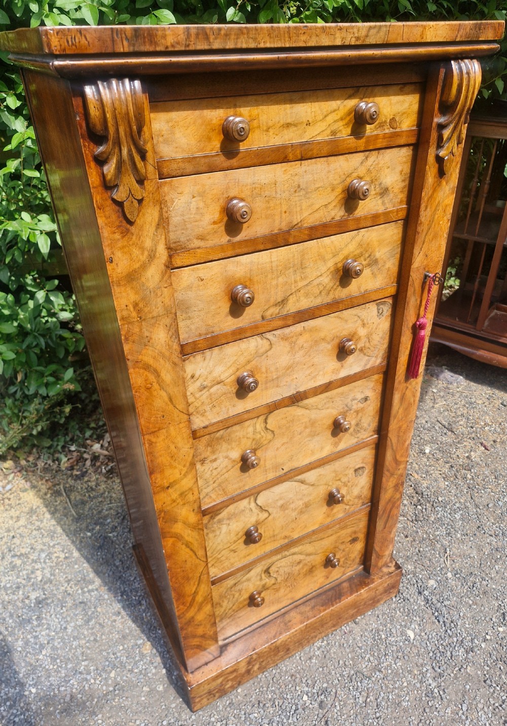 A tall Victorian walnut Wellington chest featuring seven stacked drawers with turned wooden knobs, carved upper corbels, and a side locking pilaster bar. View VII
