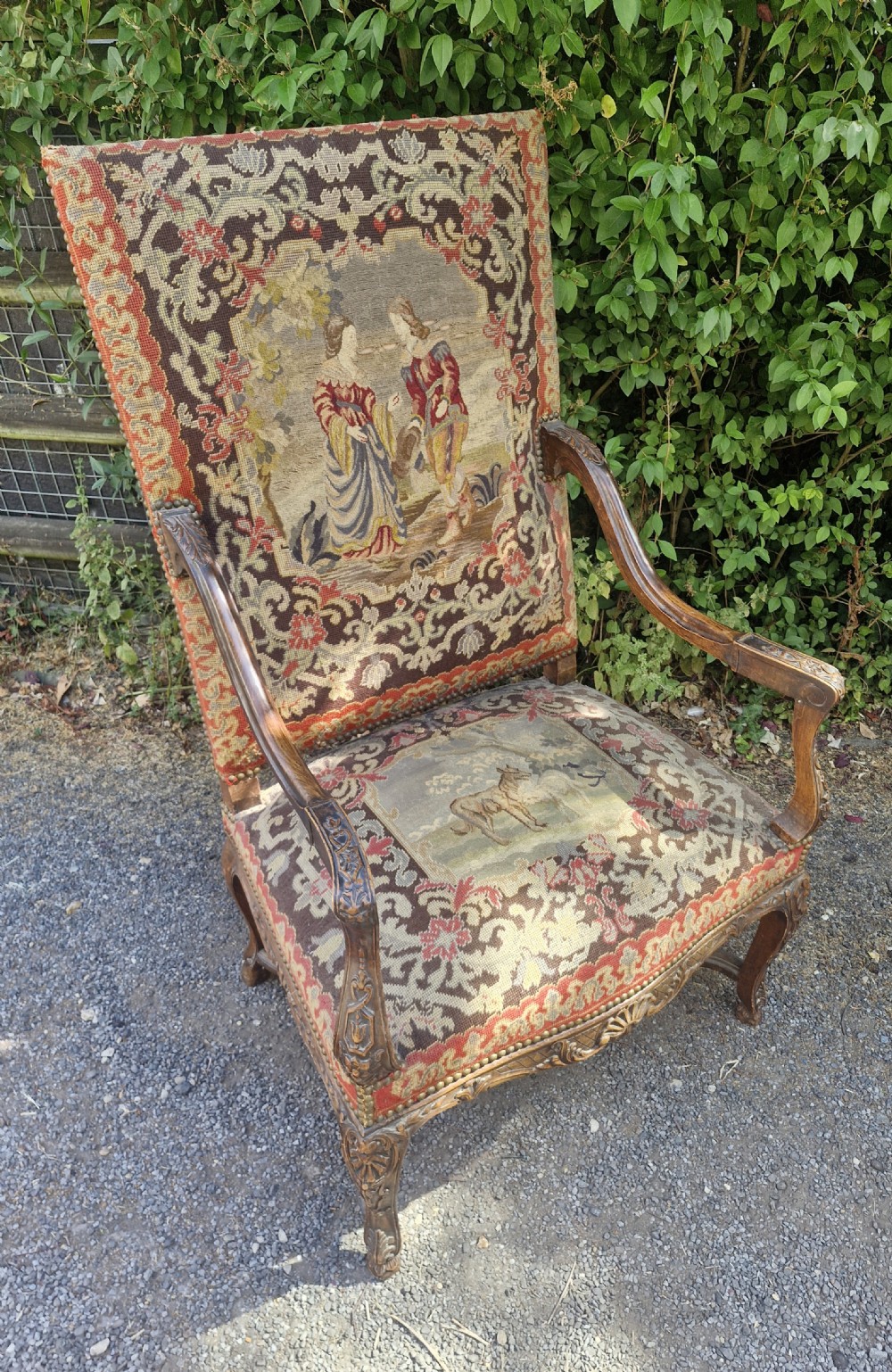 A late nineteenth-century high-back armchair featuring an intricately carved timber frame, scroll arms, cabriole legs, and pictorial needlework upholstery trimmed with brass studs. View IV