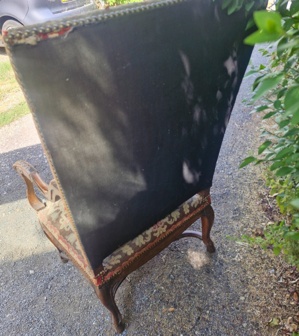 A late nineteenth-century high-back armchair featuring an intricately carved timber frame, scroll arms, cabriole legs, and pictorial needlework upholstery trimmed with brass studs. View V