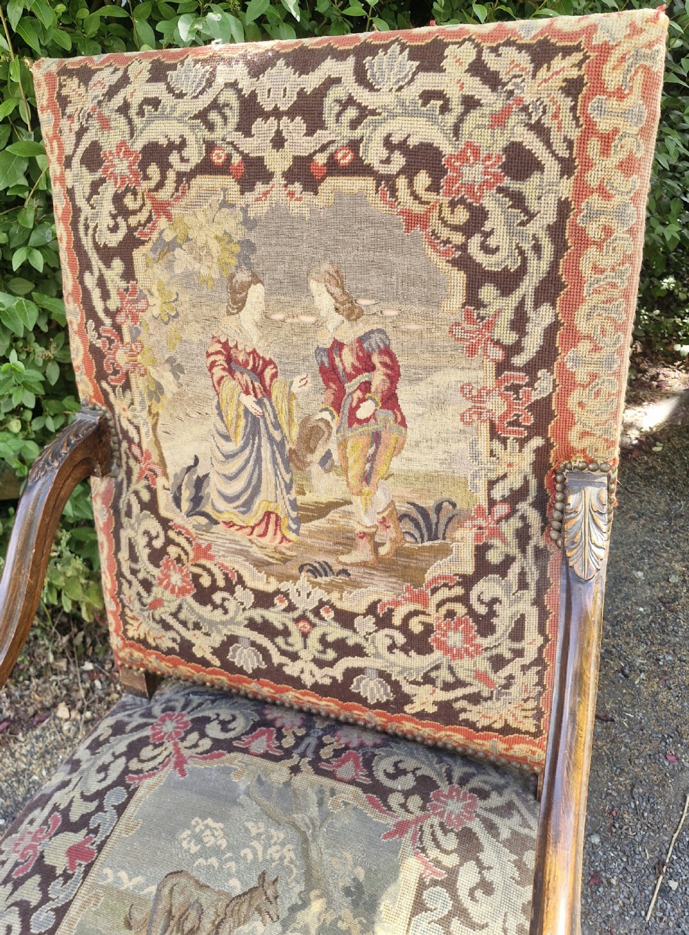 A late nineteenth-century high-back armchair featuring an intricately carved timber frame, scroll arms, cabriole legs, and pictorial needlework upholstery trimmed with brass studs. View IX