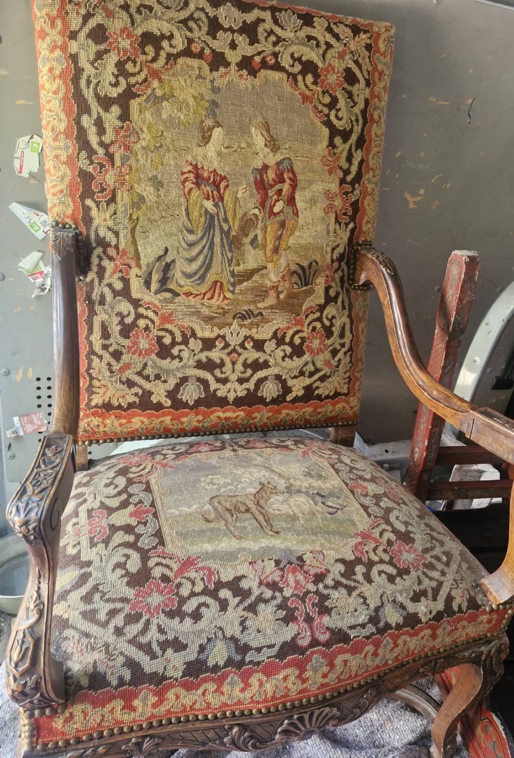 A late nineteenth-century high-back armchair featuring an intricately carved timber frame, scroll arms, cabriole legs, and pictorial needlework upholstery trimmed with brass studs. View XII