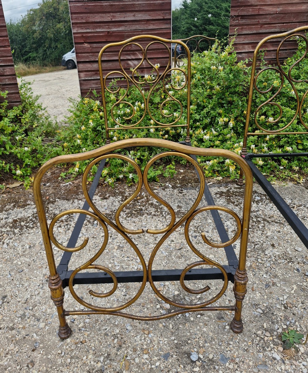 A matching pair of brass single bedsteads featuring decorative curved scrollwork headboards and footboards with black iron side rails. View V
