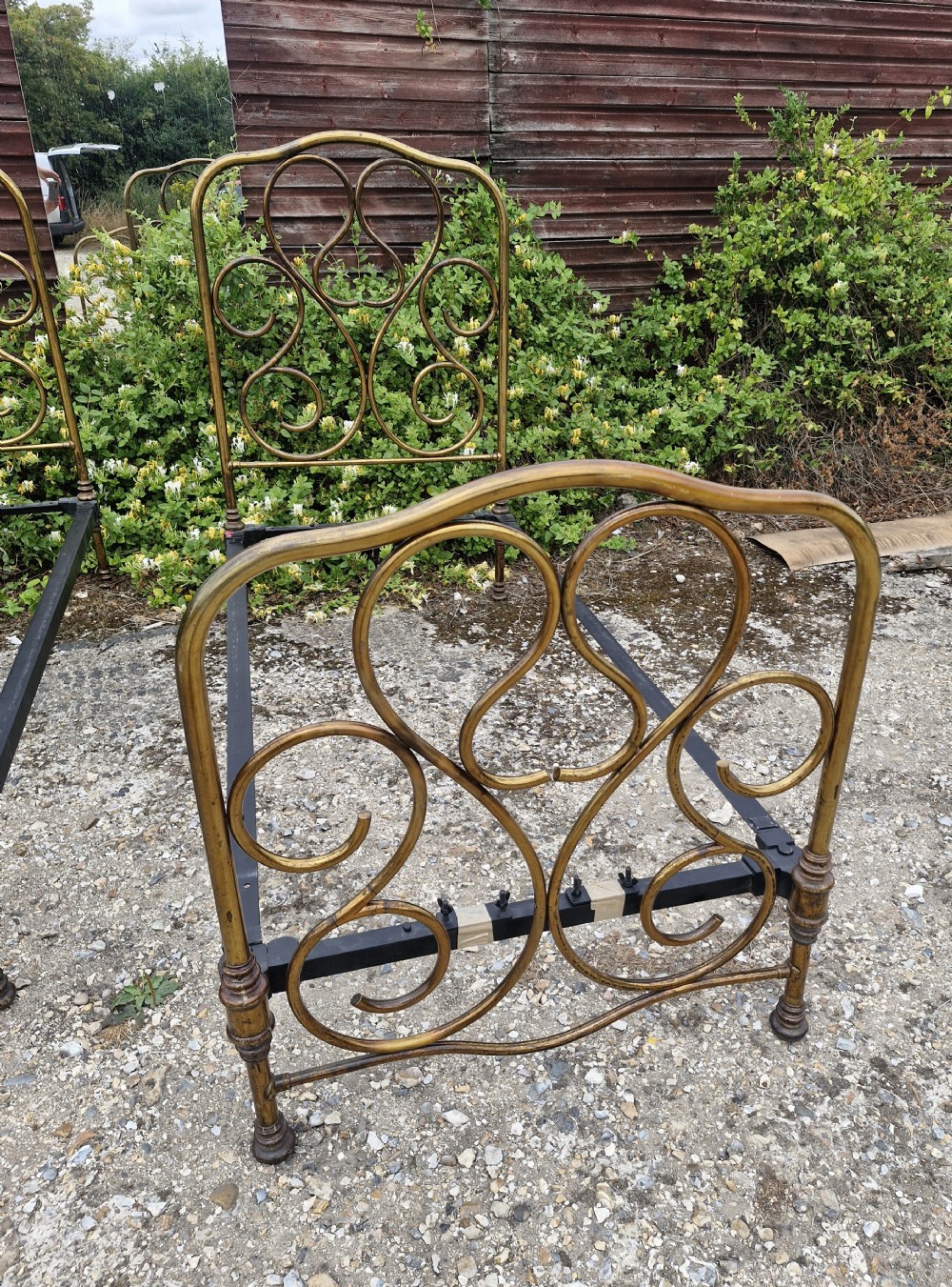 A matching pair of brass single bedsteads featuring decorative curved scrollwork headboards and footboards with black iron side rails. View VI