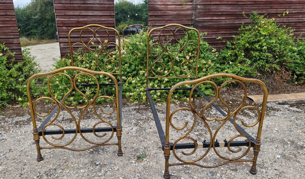 A matching pair of brass single bedsteads featuring decorative curved scrollwork headboards and footboards with black iron side rails. View VII