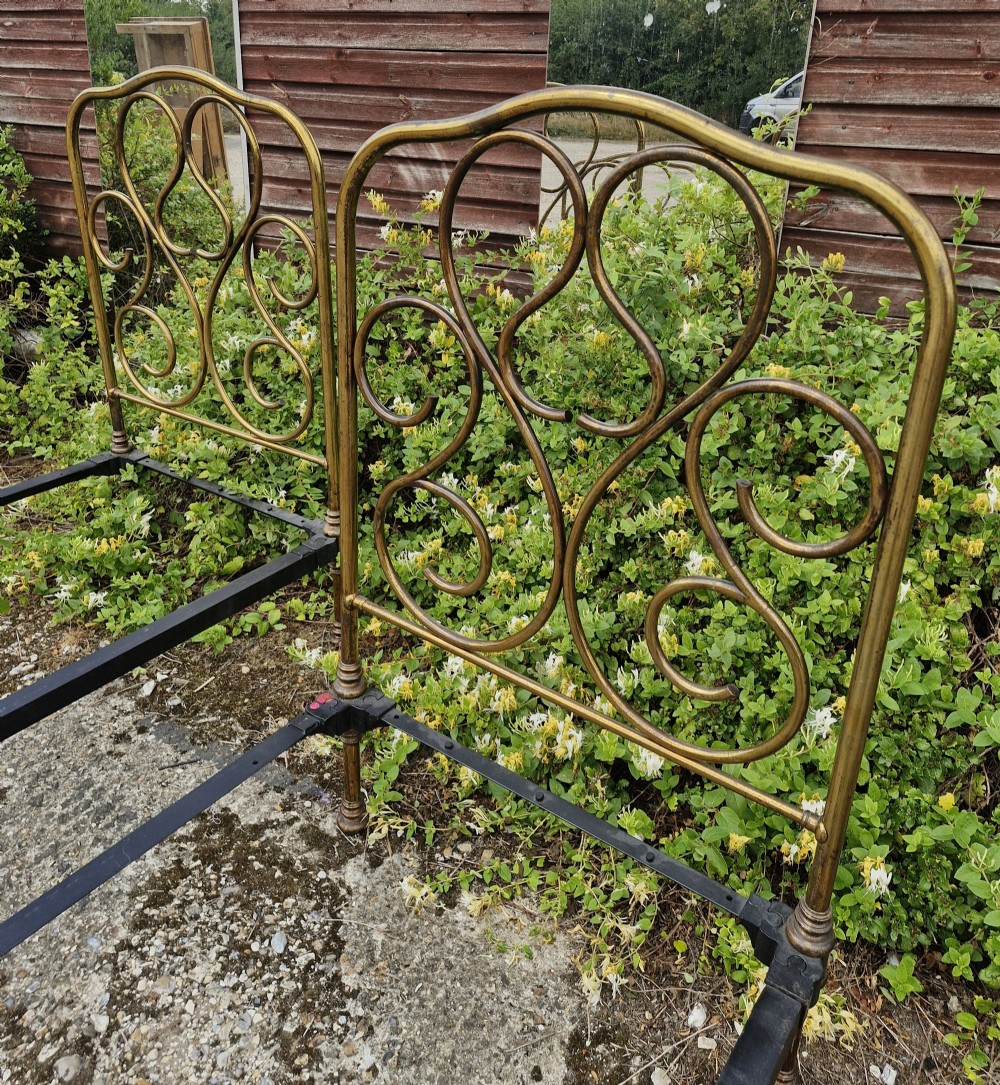 A matching pair of brass single bedsteads featuring decorative curved scrollwork headboards and footboards with black iron side rails. View VIII