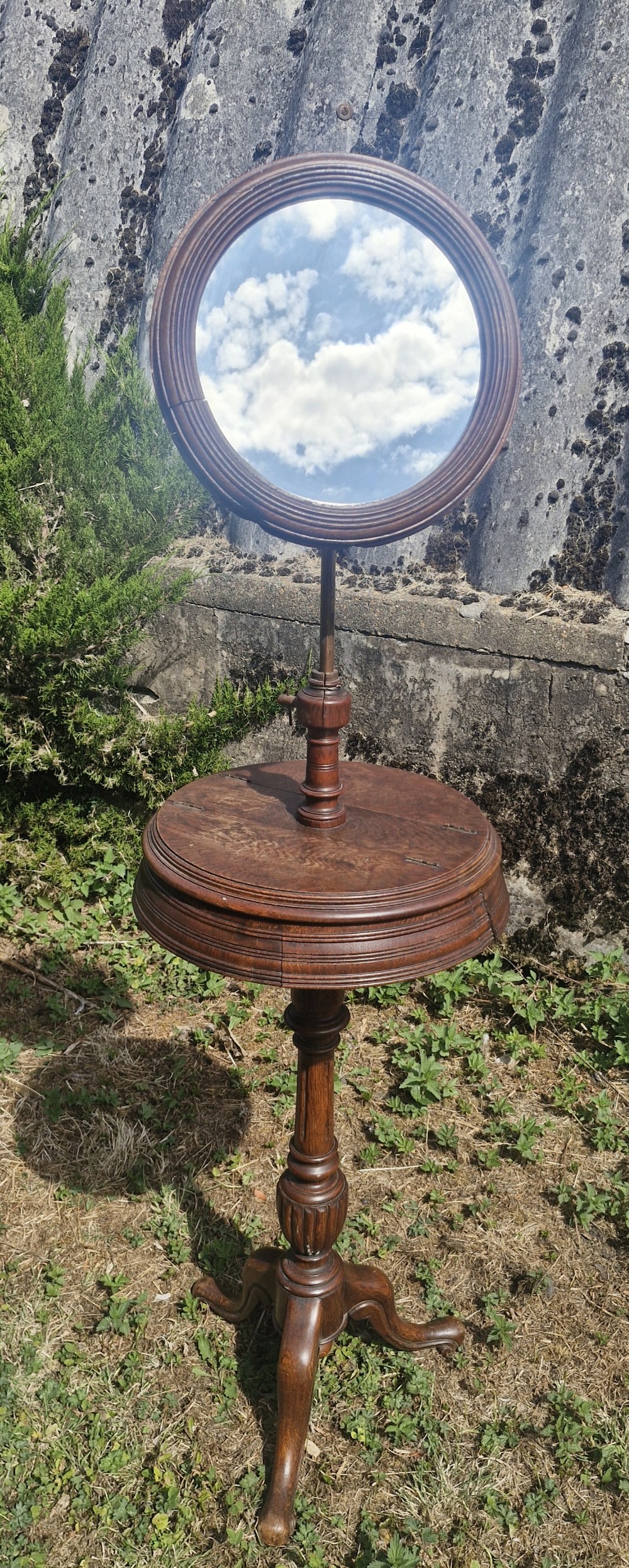 A Victorian dark oak shaving stand featuring an adjustable circular mirror mounted above a round surface, supported by a turned pedestal and tripod cabriole legs.