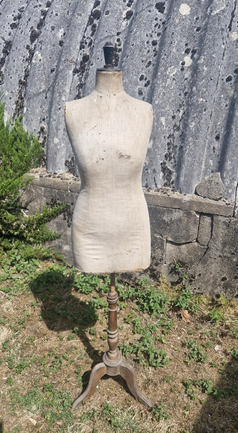 An early 20th-century dressmakers mannequin with a distressed beige linen torso on a turned wooden tripod stand.