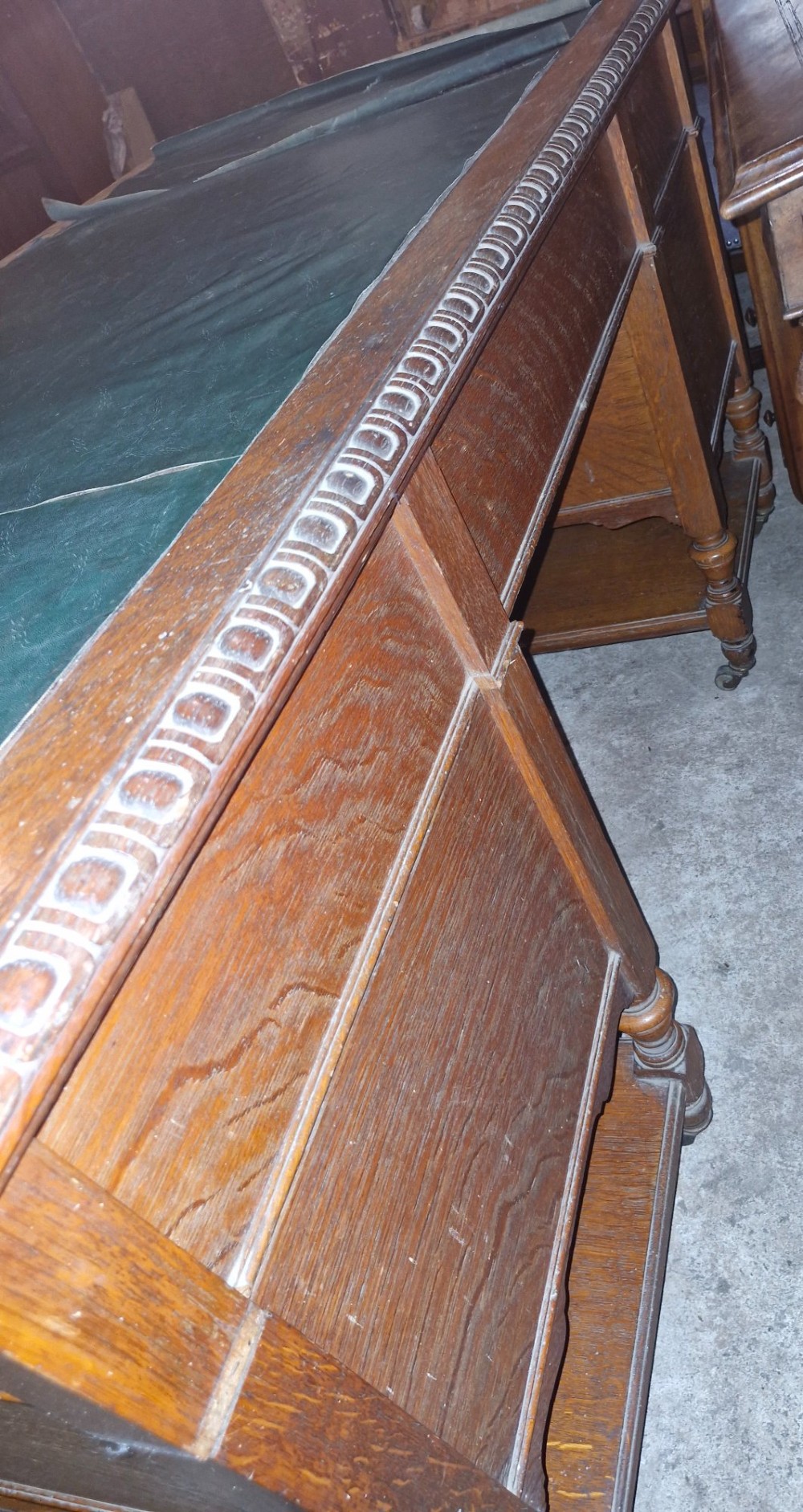 An Edwardian carved oak kneehole pedestal desk featuring a green leather writing insert, multiple drawers with brass swing handles, carved borders, and turned legs set on castors. View VI