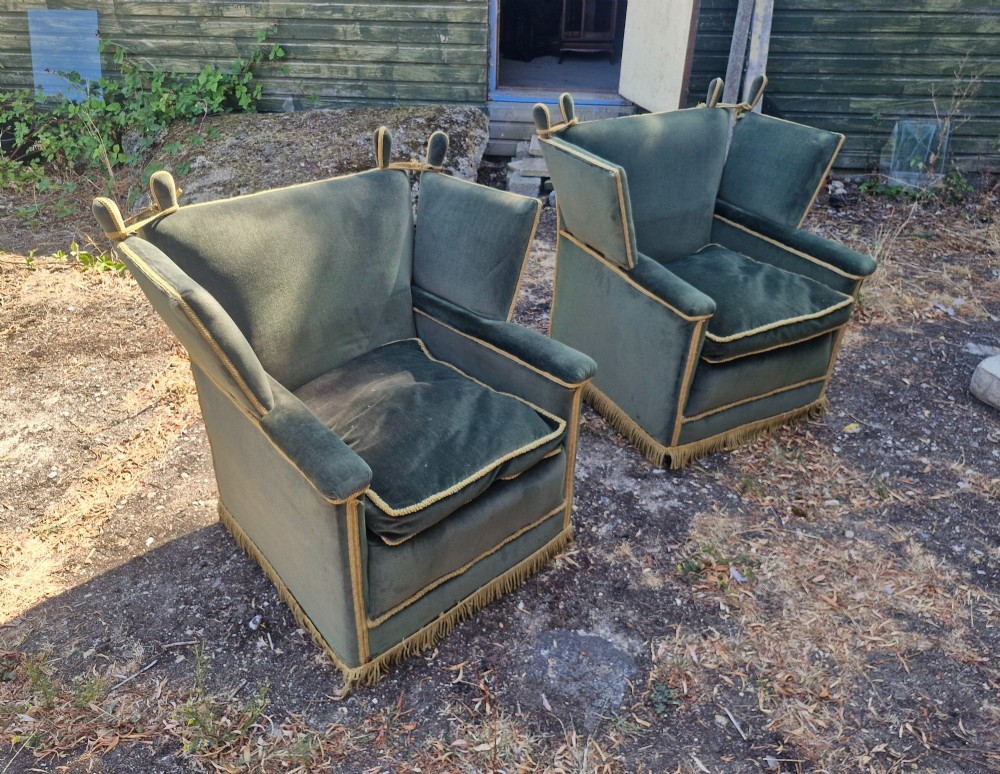 A pair of olive green velvet Knole armchairs featuring drop-side arms with finial ties, gold piping, and lower fringe trim.