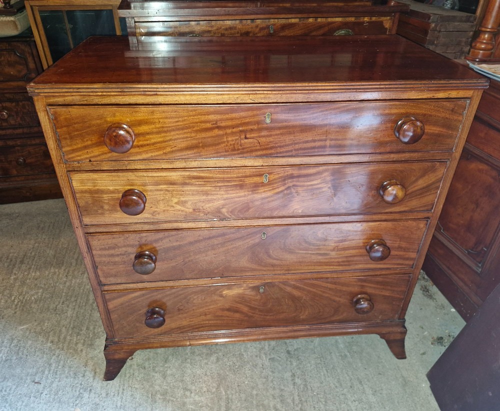An early nineteenth-century mahogany chest of drawers featuring four graduated drawers with turned wooden knobs and bracket feet.