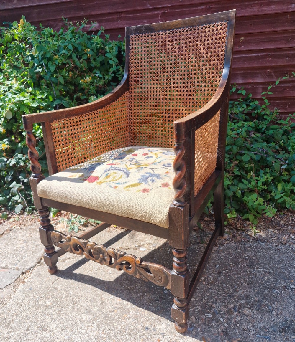 A dark oak bergere armchair featuring woven cane back and side panels, barley twist arm supports, a carved front stretcher, and a floral tapestry seat cushion. View V