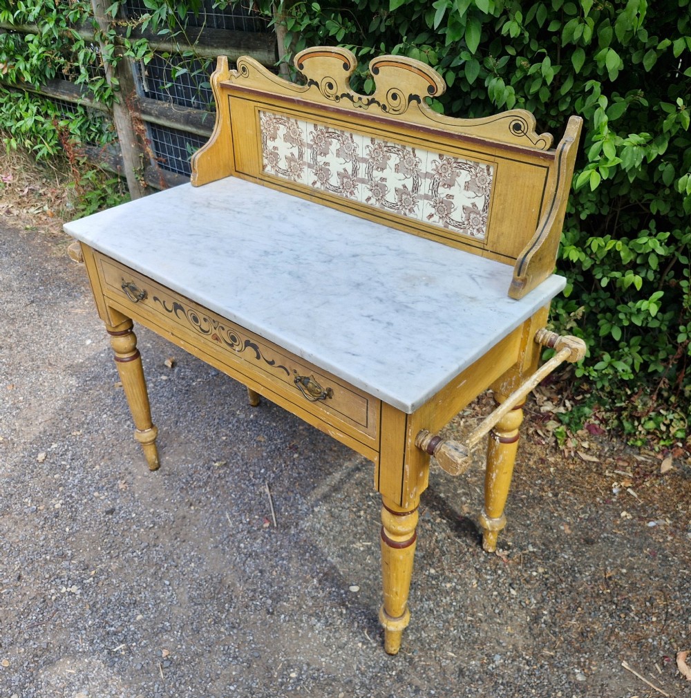 A late Victorian yellow painted washstand featuring a white marble top, ceramic tiled splashback with floral motifs, a single drawer, and turned legs. View II