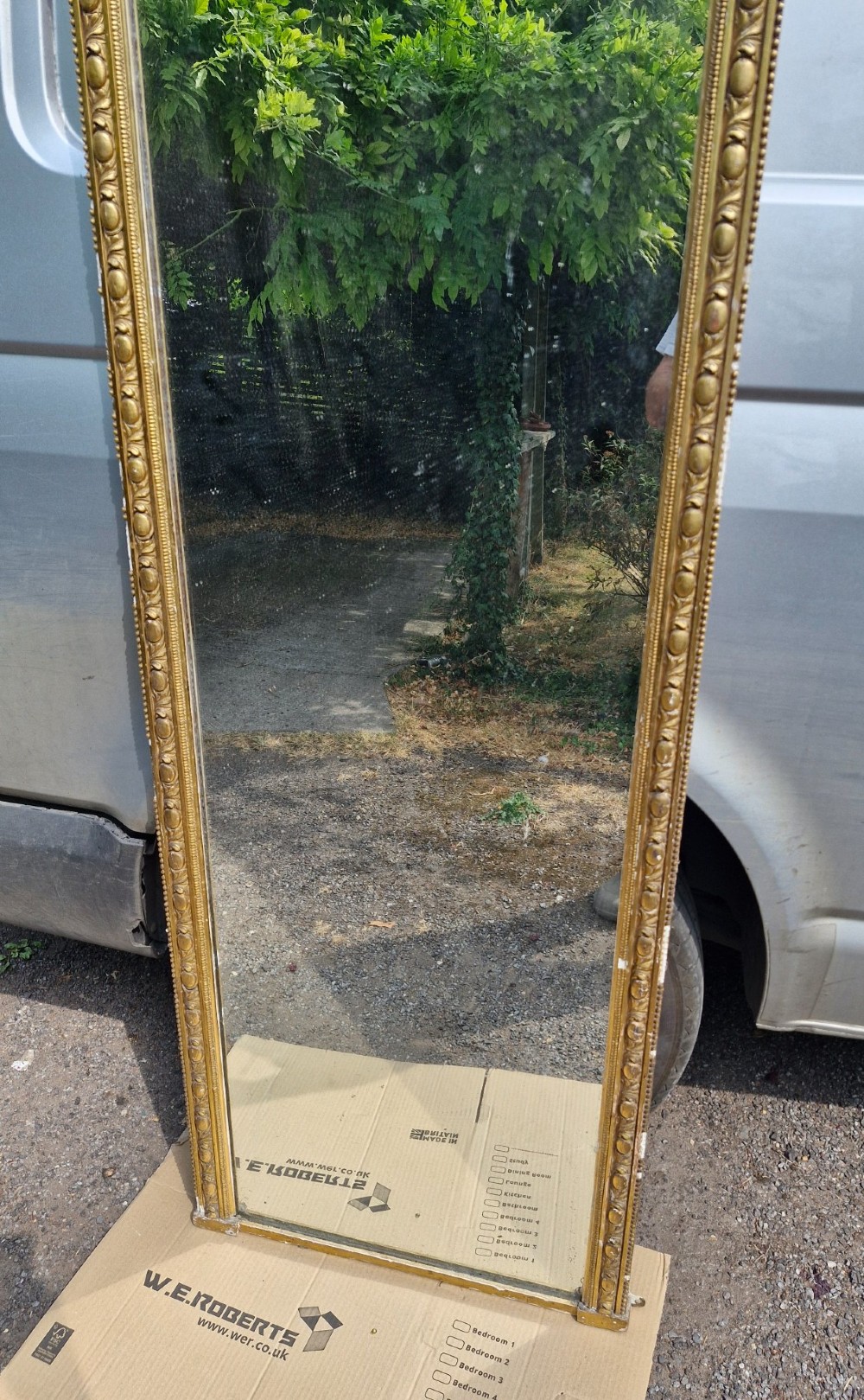 A tall Victorian mirror featuring an arched giltwood frame decorated with bead moulding and an ornate cresting motif at the top. View VI