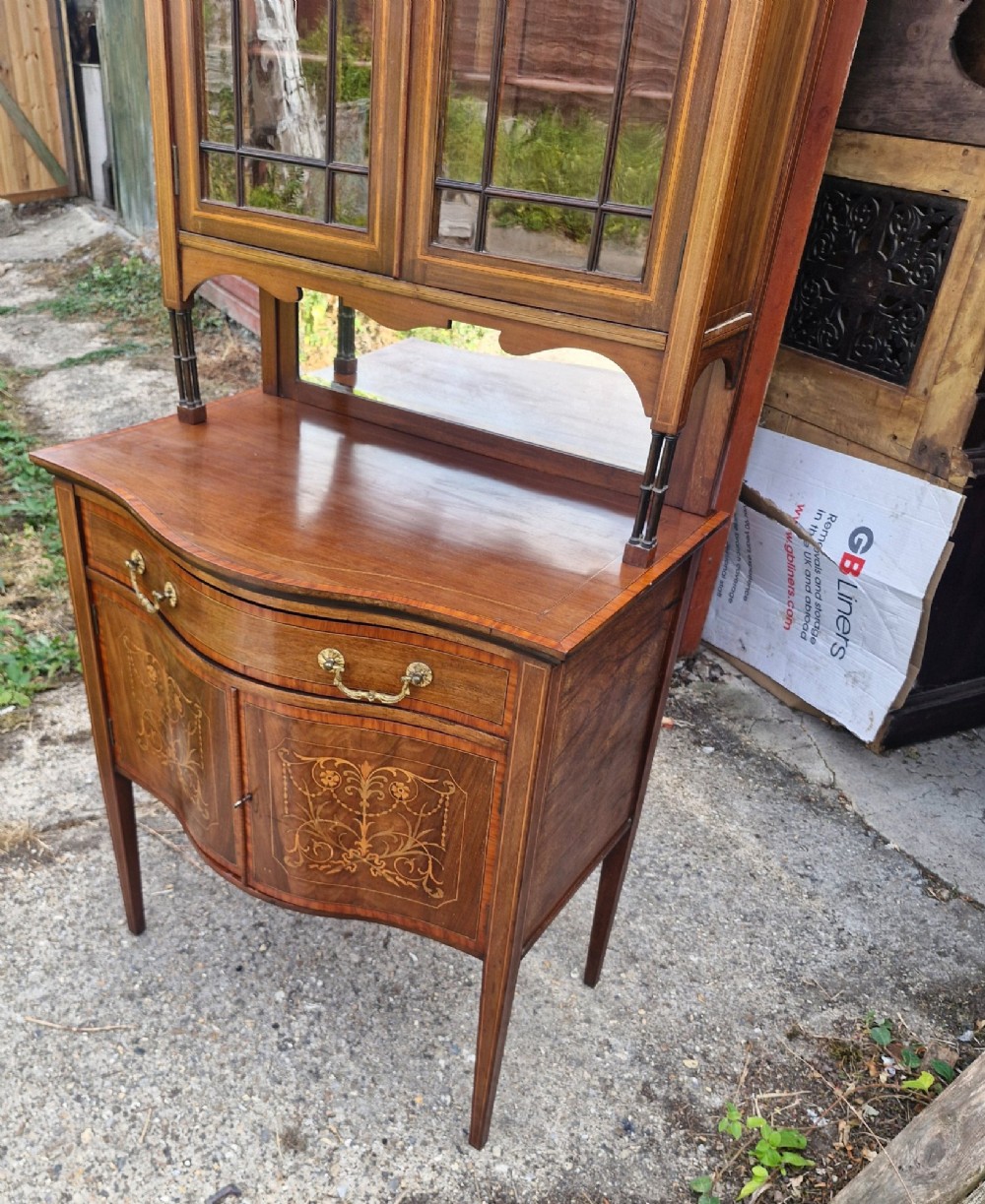 An Edwardian inlaid mahogany two-part display cabinet featuring a swan-neck pediment, glazed upper doors, a mirrored splashback, and lower cupboard doors with floral marquetry. View II