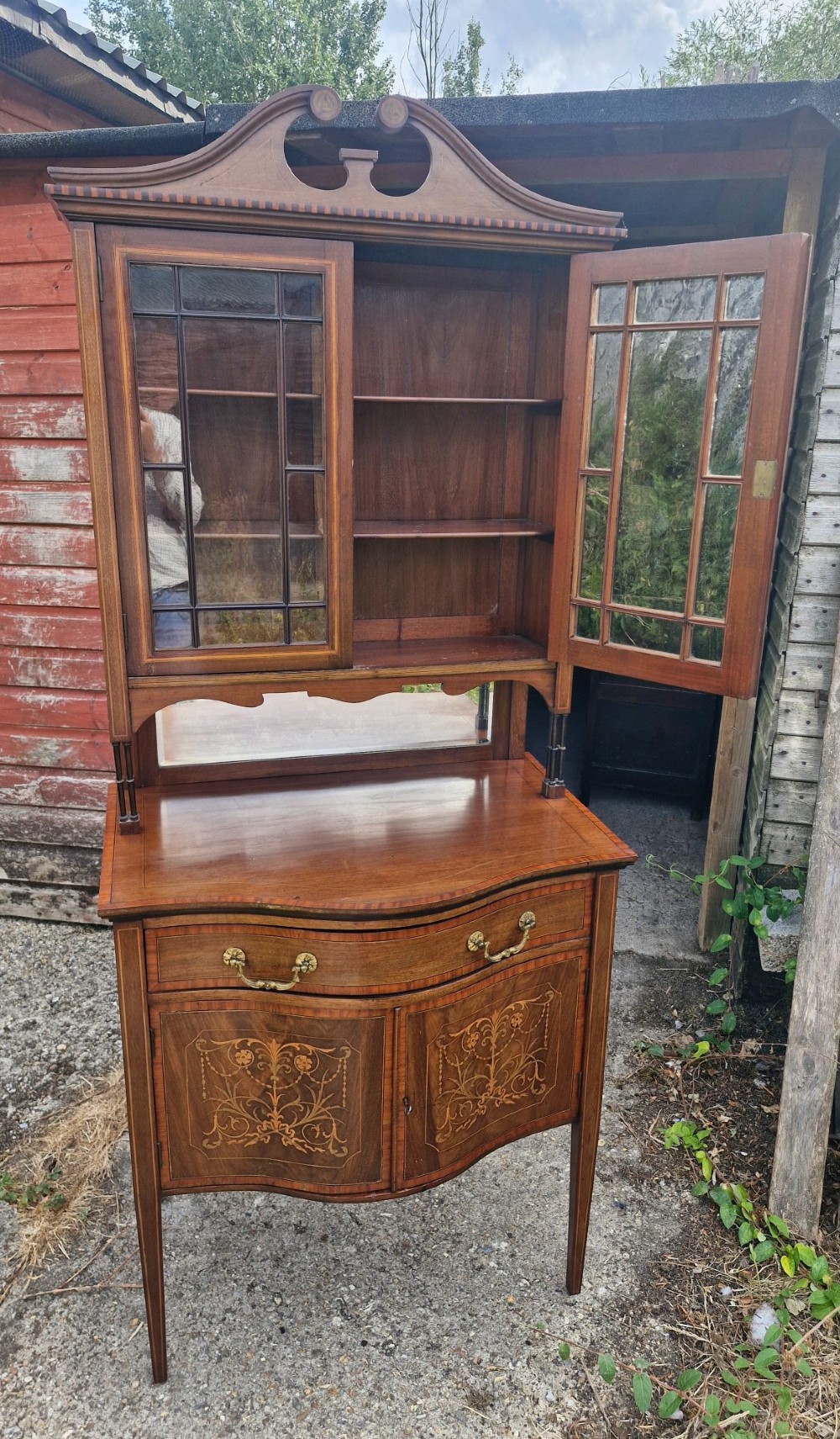 An Edwardian inlaid mahogany two-part display cabinet featuring a swan-neck pediment, glazed upper doors, a mirrored splashback, and lower cupboard doors with floral marquetry. View VII