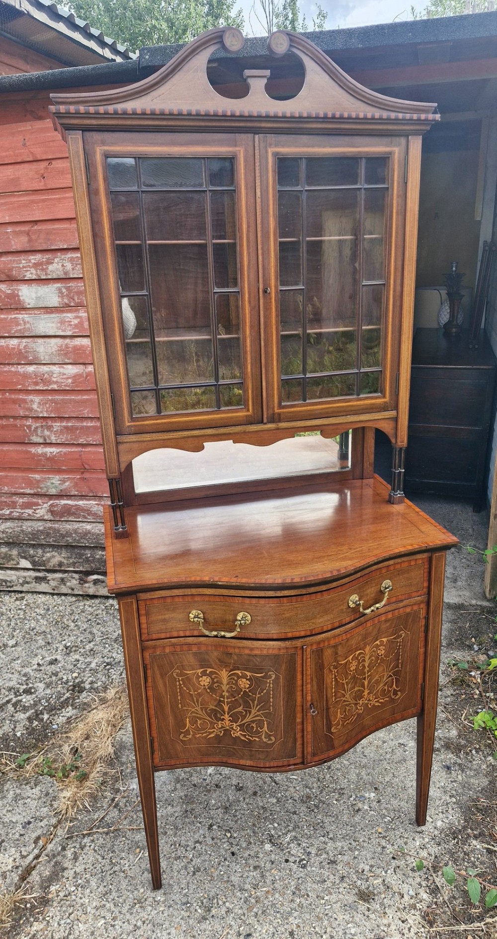 An Edwardian inlaid mahogany two-part display cabinet featuring a swan-neck pediment, glazed upper doors, a mirrored splashback, and lower cupboard doors with floral marquetry. View IX