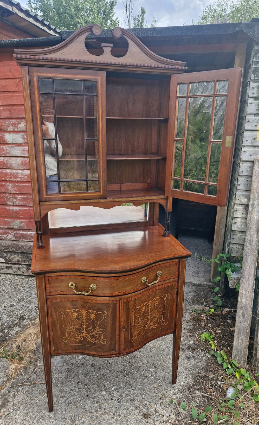 An Edwardian inlaid mahogany two-part display cabinet featuring a swan-neck pediment, glazed upper doors, a mirrored splashback, and lower cupboard doors with floral marquetry. View XIV