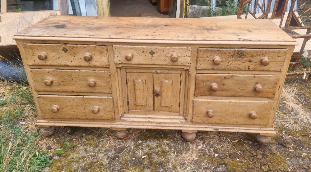 A wide Victorian pine dresser base featuring multiple drawers with turned wooden handles flanking a central double cupboard, resting on turned feet.
