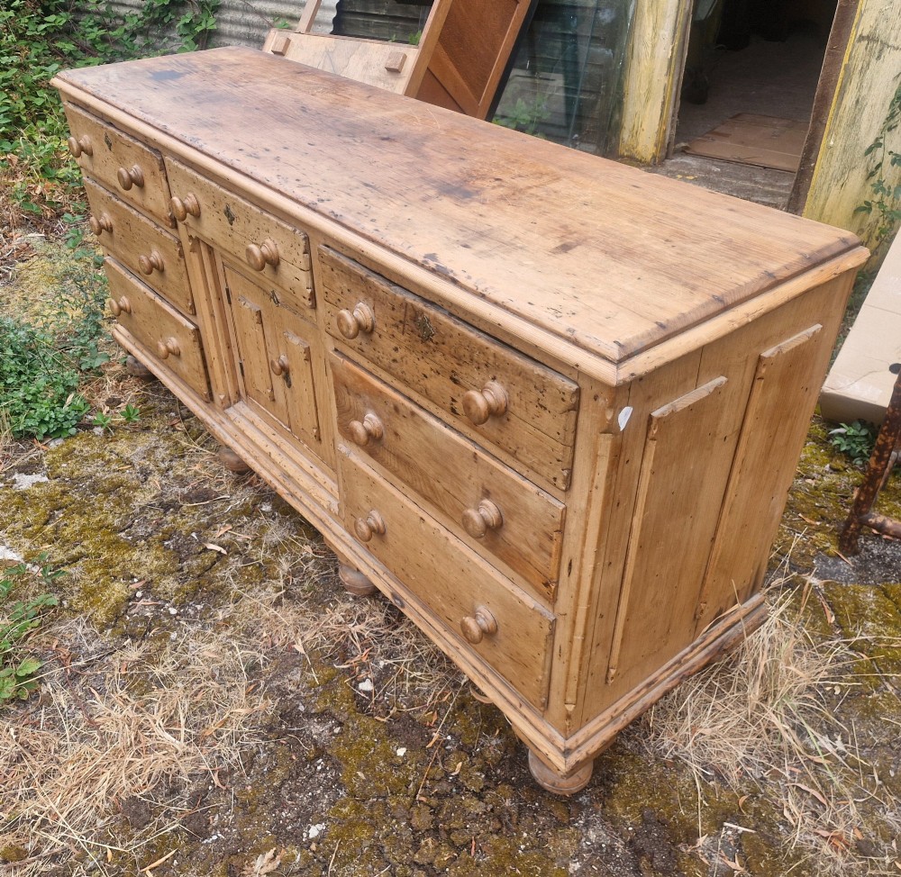 A wide Victorian pine dresser base featuring multiple drawers with turned wooden handles flanking a central double cupboard, resting on turned feet. View II