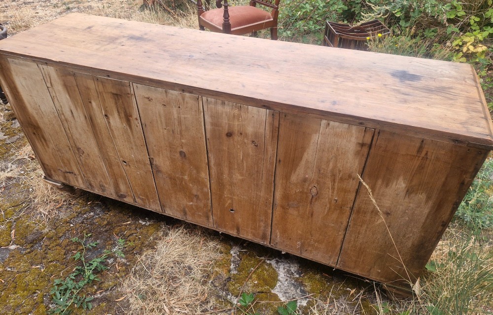 A wide Victorian pine dresser base featuring multiple drawers with turned wooden handles flanking a central double cupboard, resting on turned feet. View III