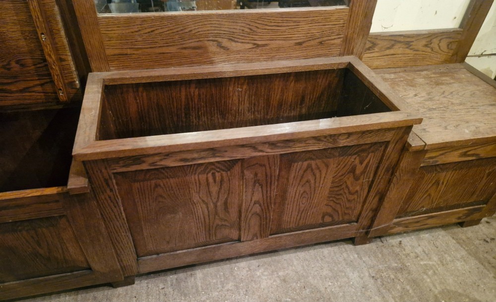 A large dark oak hall stand featuring a central arched mirror flanked by brass coat hooks, set above built-in storage boxes and a central trough base. View II