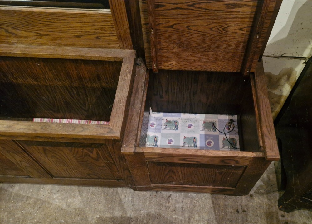 A large dark oak hall stand featuring a central arched mirror flanked by brass coat hooks, set above built-in storage boxes and a central trough base. View V