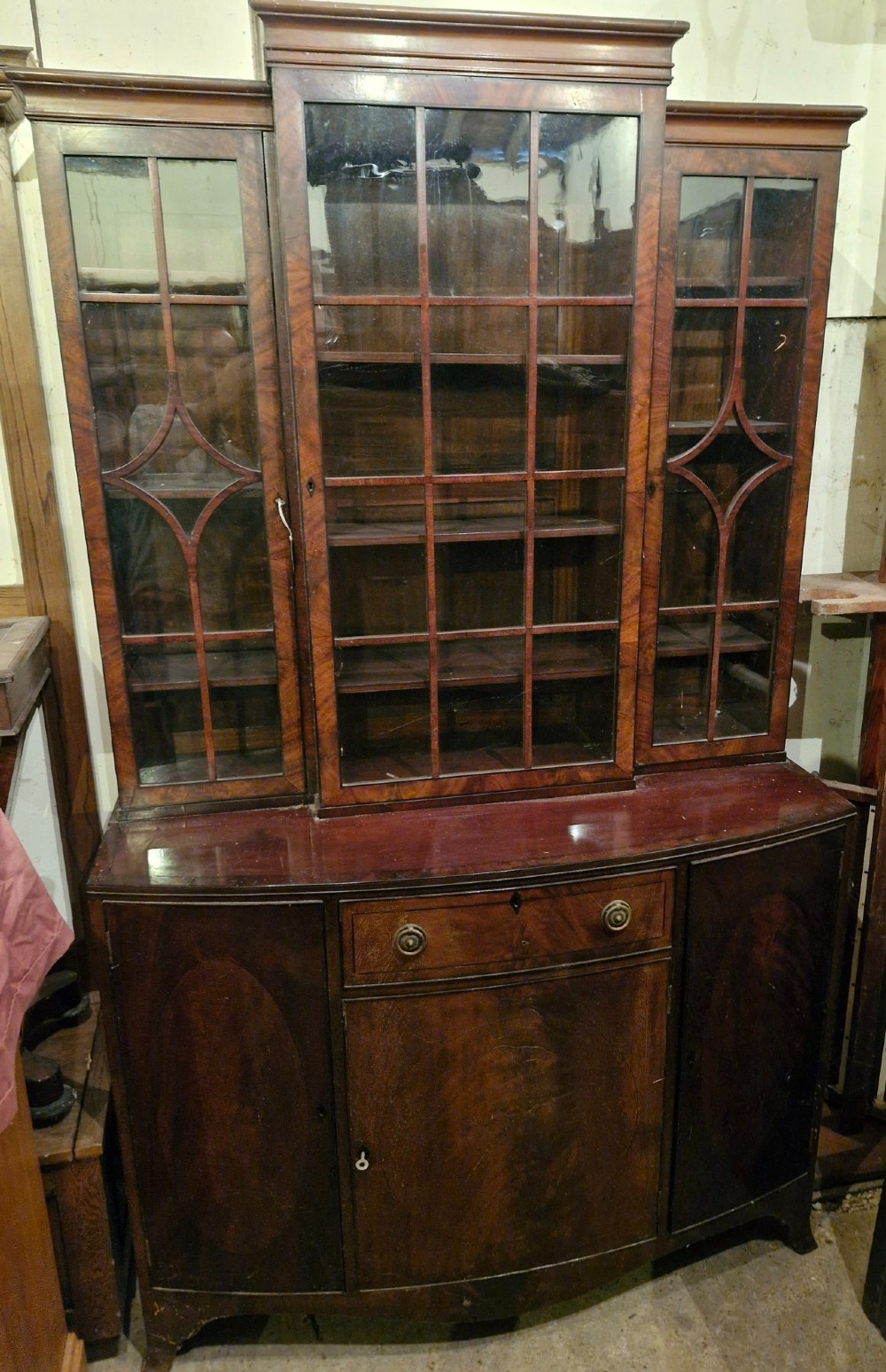 An early twentieth century dark mahogany breakfront bookcase cabinet featuring glazed doors with geometric astragal glazing bars above a cupboard base. View II