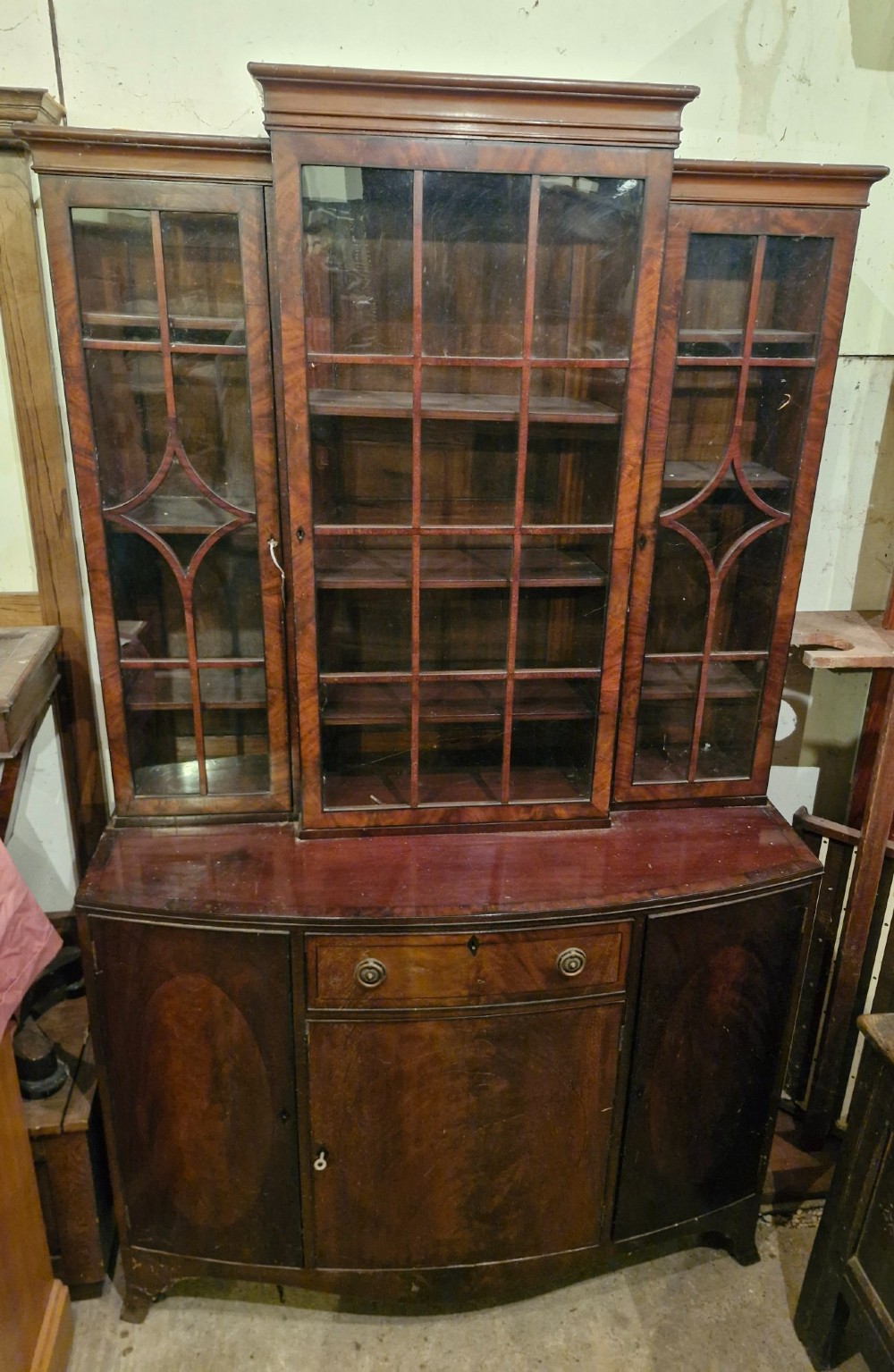 An early twentieth century dark mahogany breakfront bookcase cabinet featuring glazed doors with geometric astragal glazing bars above a cupboard base. View V