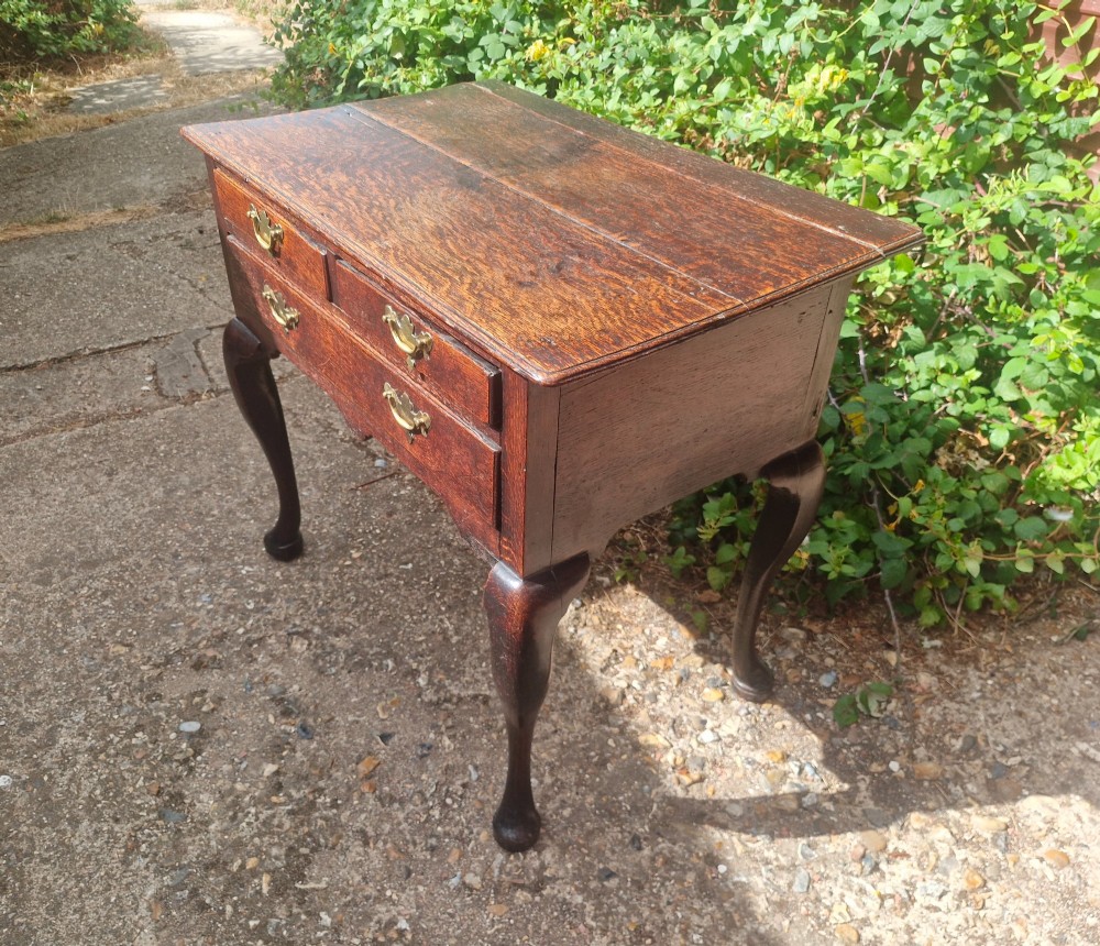 A mid-18th century dark oak side table with three drawers, brass handles, and cabriole legs on pad feet. View V