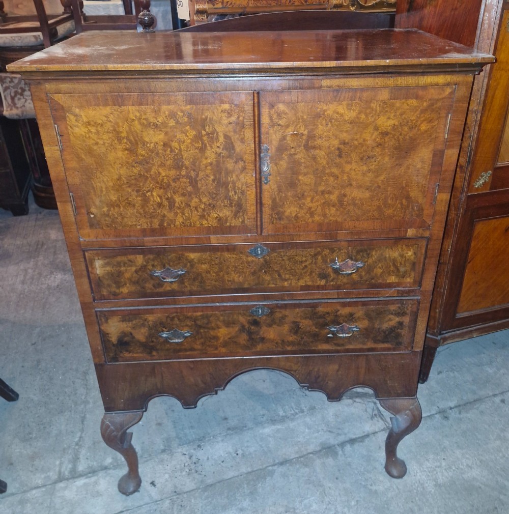 An early 20th-century burr walnut cabinet chest featuring twin upper doors over two drawers, resting on a shaped apron with carved cabriole legs.