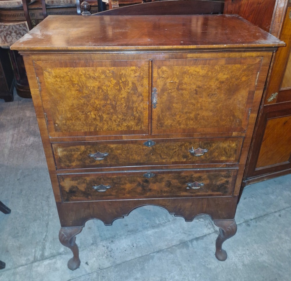 An early 20th-century burr walnut cabinet chest featuring twin upper doors over two drawers, resting on a shaped apron with carved cabriole legs. View IV