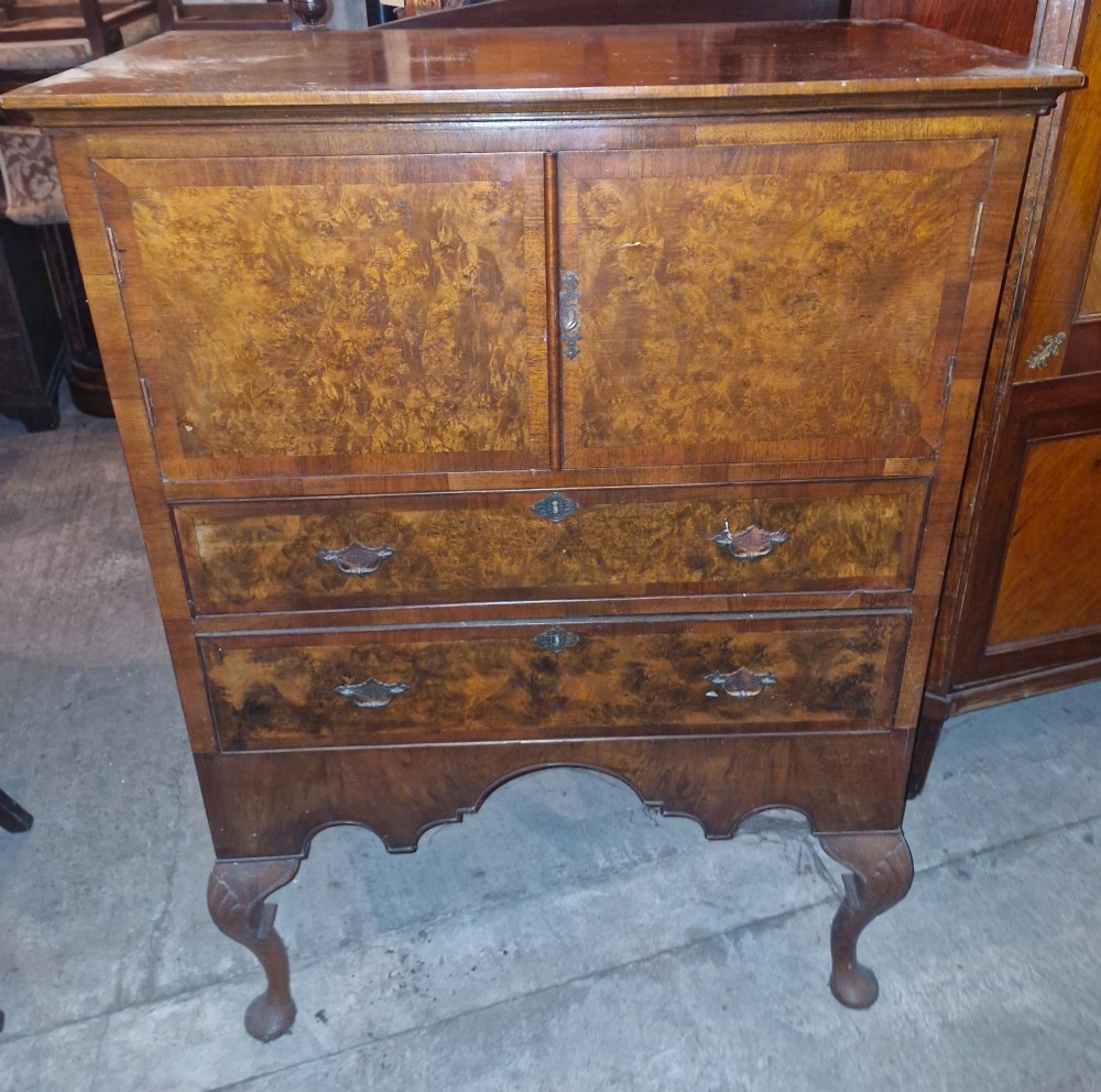 An early 20th-century burr walnut cabinet chest featuring twin upper doors over two drawers, resting on a shaped apron with carved cabriole legs. View V