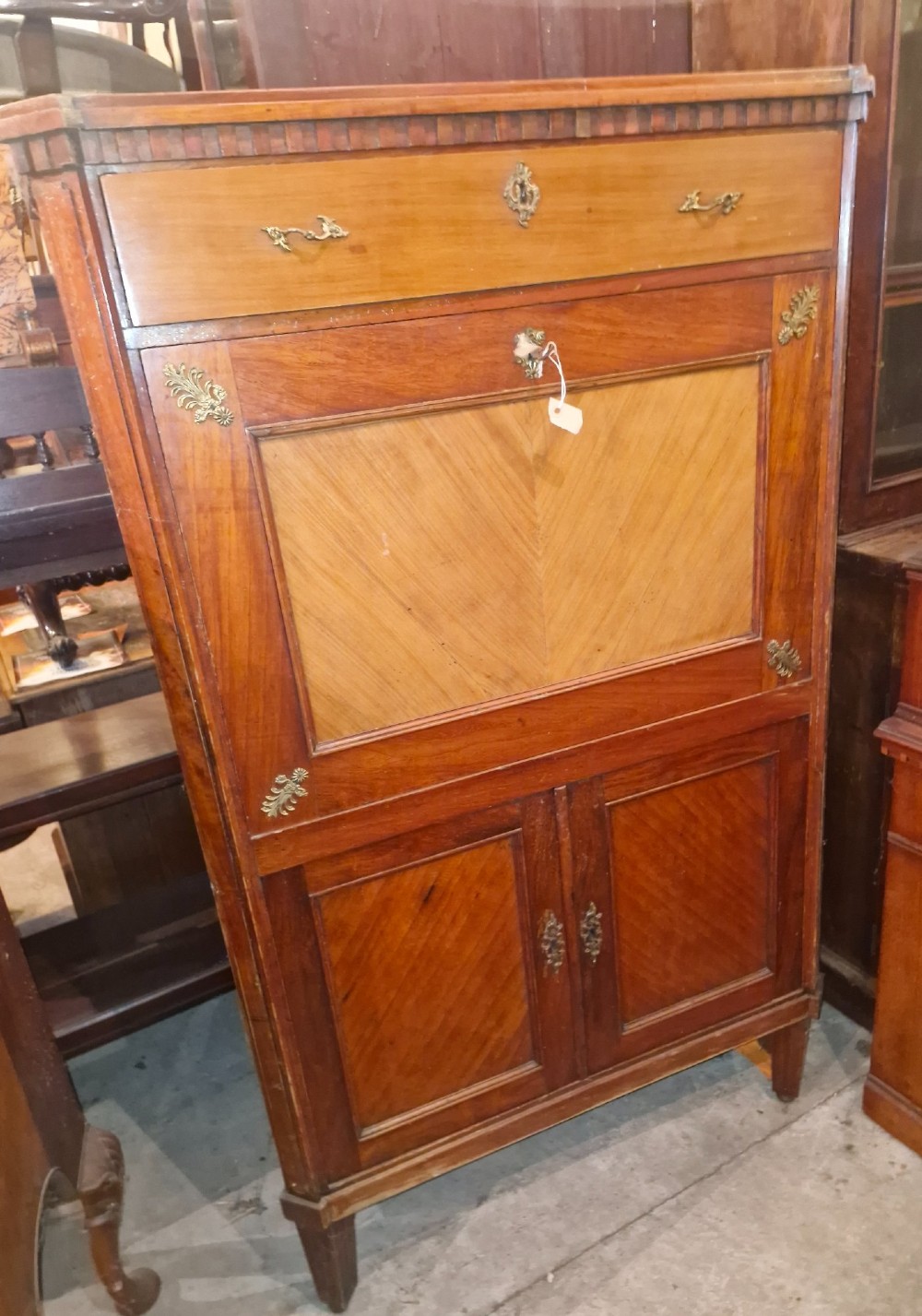 Antique mahogany secretaire cocktail cabinet featuring chevron wood veneer inlays, brass corner mounts, drop-front panel, upper drawer, and lower double doors.