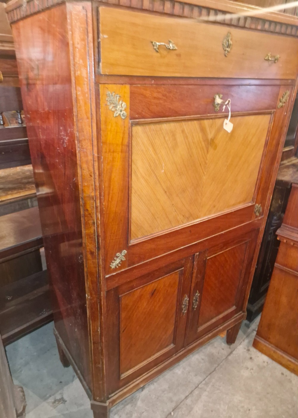 Antique mahogany secretaire cocktail cabinet featuring chevron wood veneer inlays, brass corner mounts, drop-front panel, upper drawer, and lower double doors. View VI