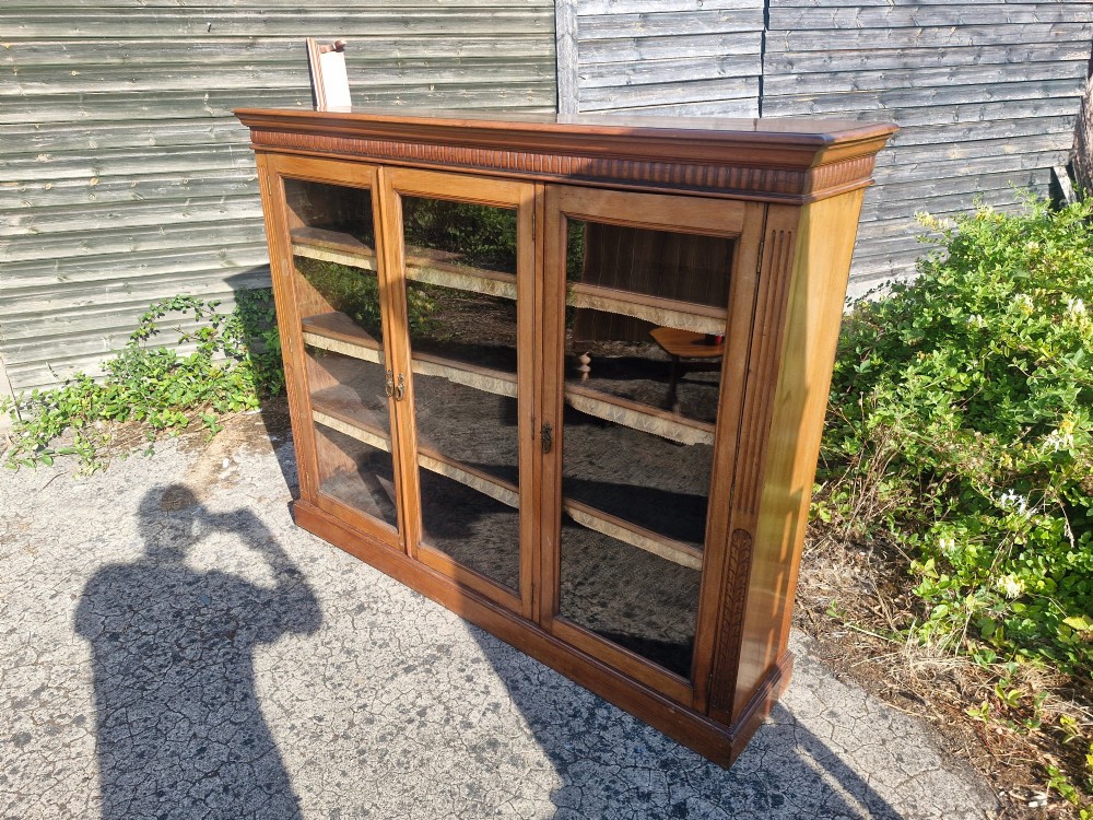 A late Victorian mahogany glazed bookcase cabinet featuring three glass panel doors, a shaped gallery upstand, and carved fluted pilasters. View II