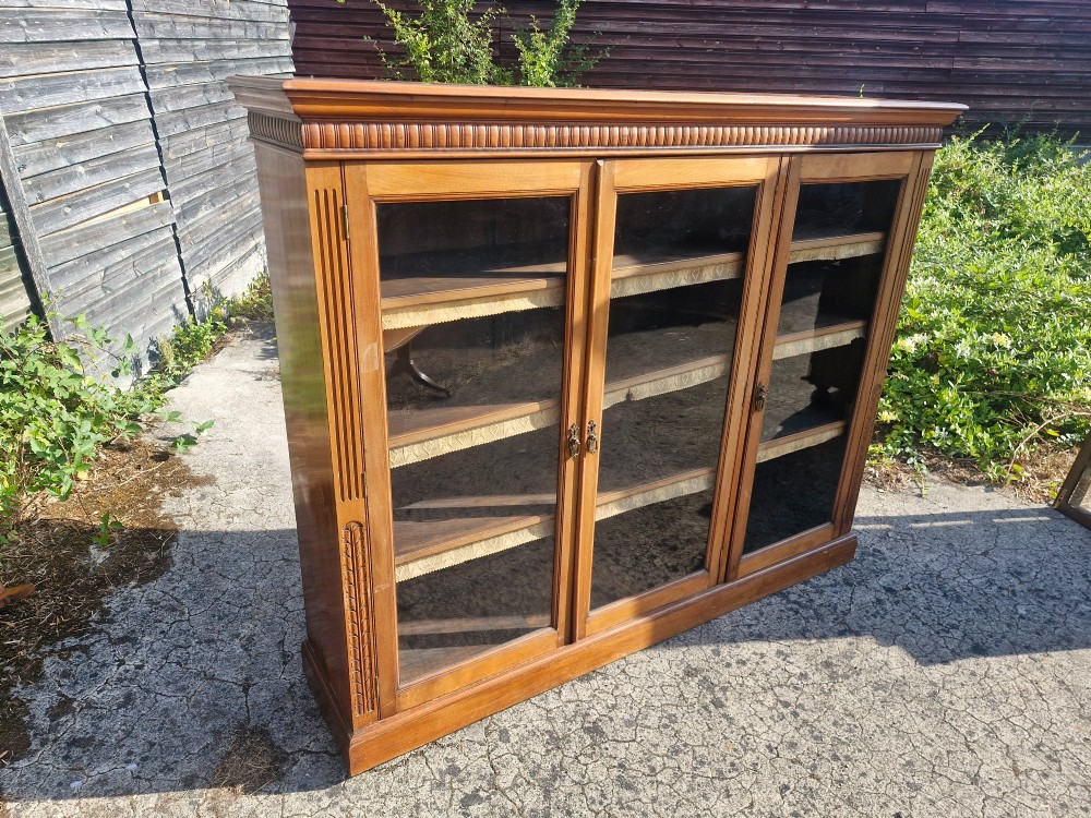 A late Victorian mahogany glazed bookcase cabinet featuring three glass panel doors, a shaped gallery upstand, and carved fluted pilasters. View III