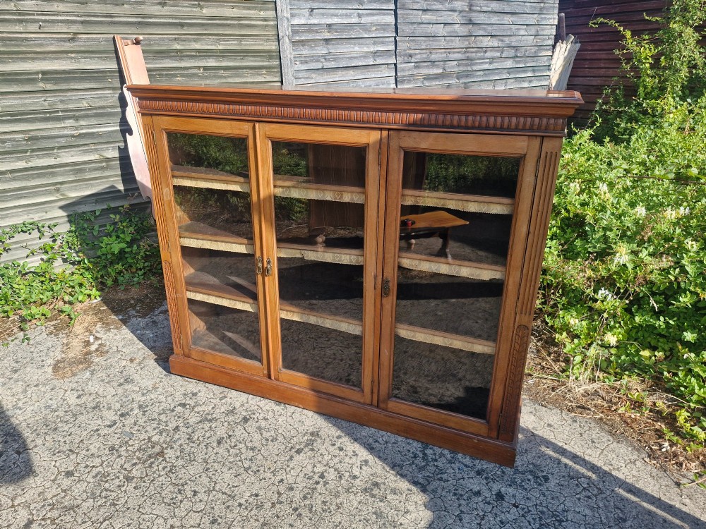 A late Victorian mahogany glazed bookcase cabinet featuring three glass panel doors, a shaped gallery upstand, and carved fluted pilasters. View IV