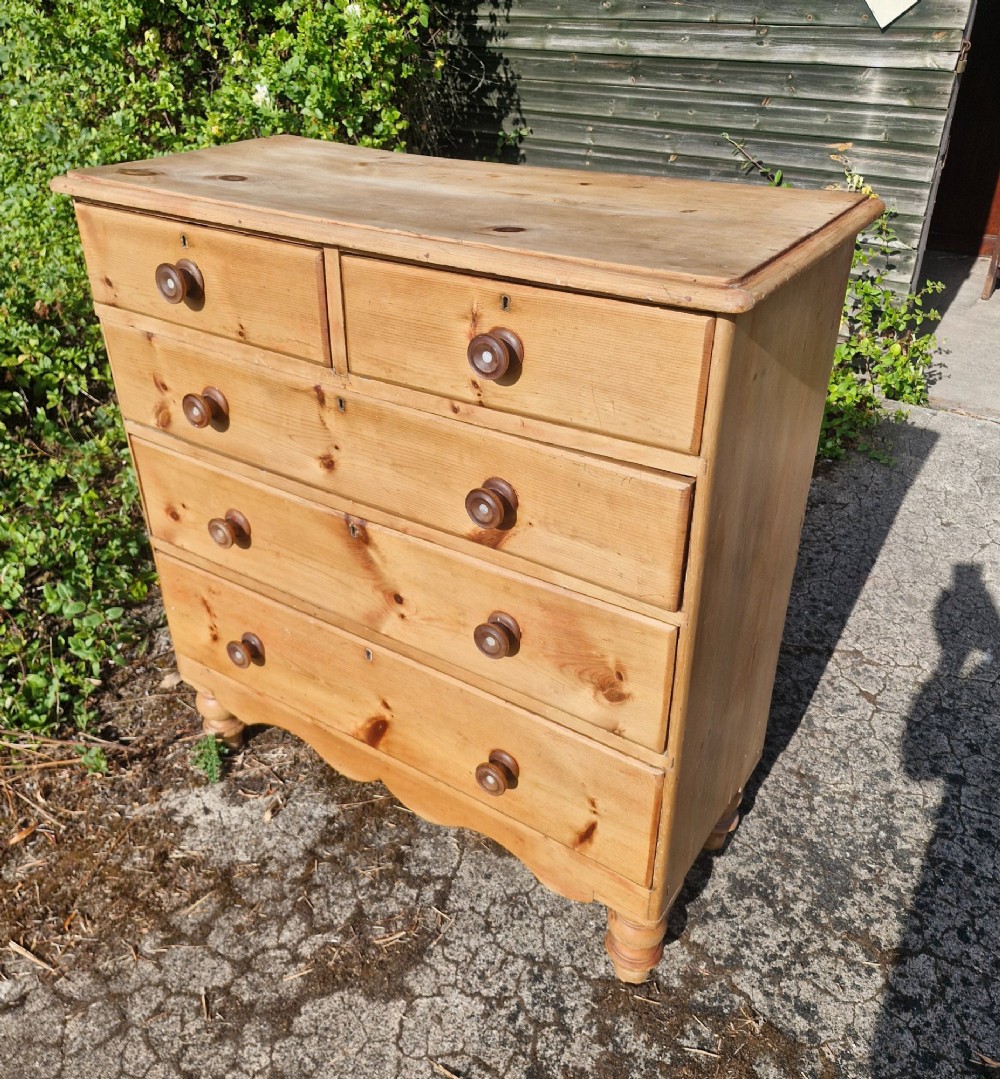 An Early Victorian pine chest of drawers featuring a two-over-three drawer configuration with turned knobs and turned feet. View V