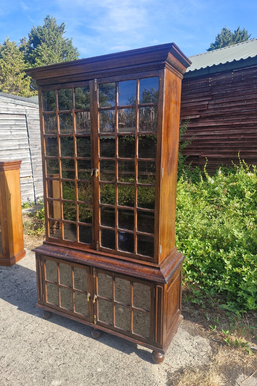 A two-part dark oak bookcase featuring upper and lower glazed double doors with multi-pane glass panels, standing on bun feet.