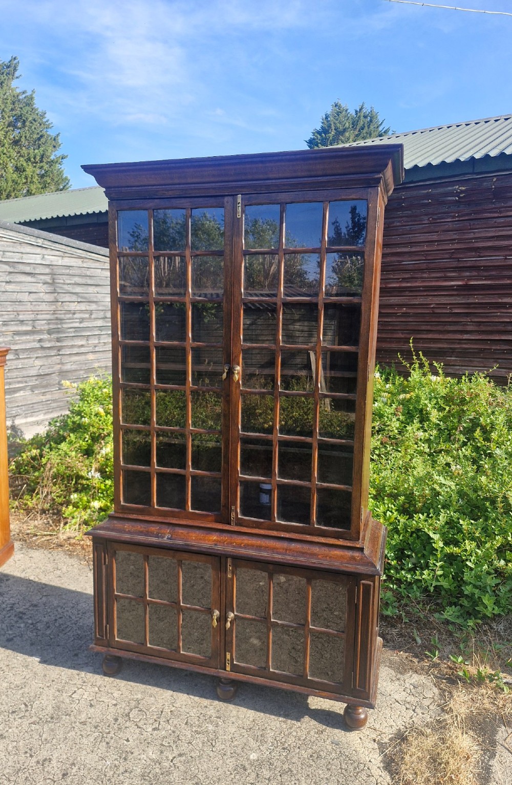 A two-part dark oak bookcase featuring upper and lower glazed double doors with multi-pane glass panels, standing on bun feet. View II