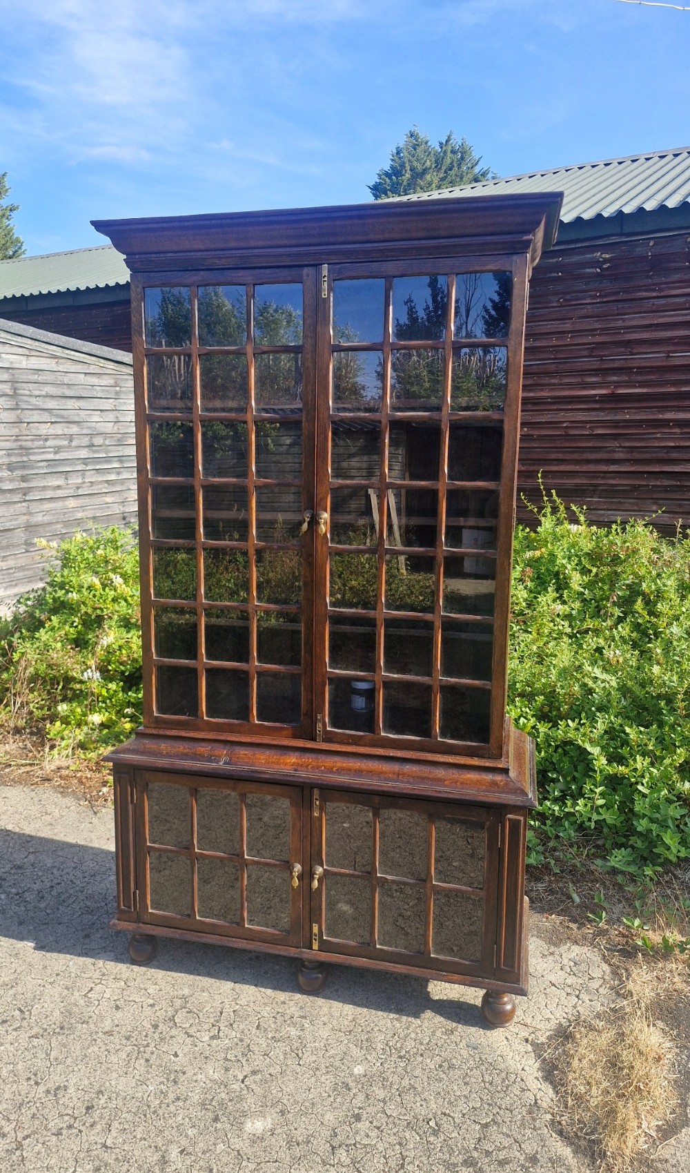 A two-part dark oak bookcase featuring upper and lower glazed double doors with multi-pane glass panels, standing on bun feet. View III