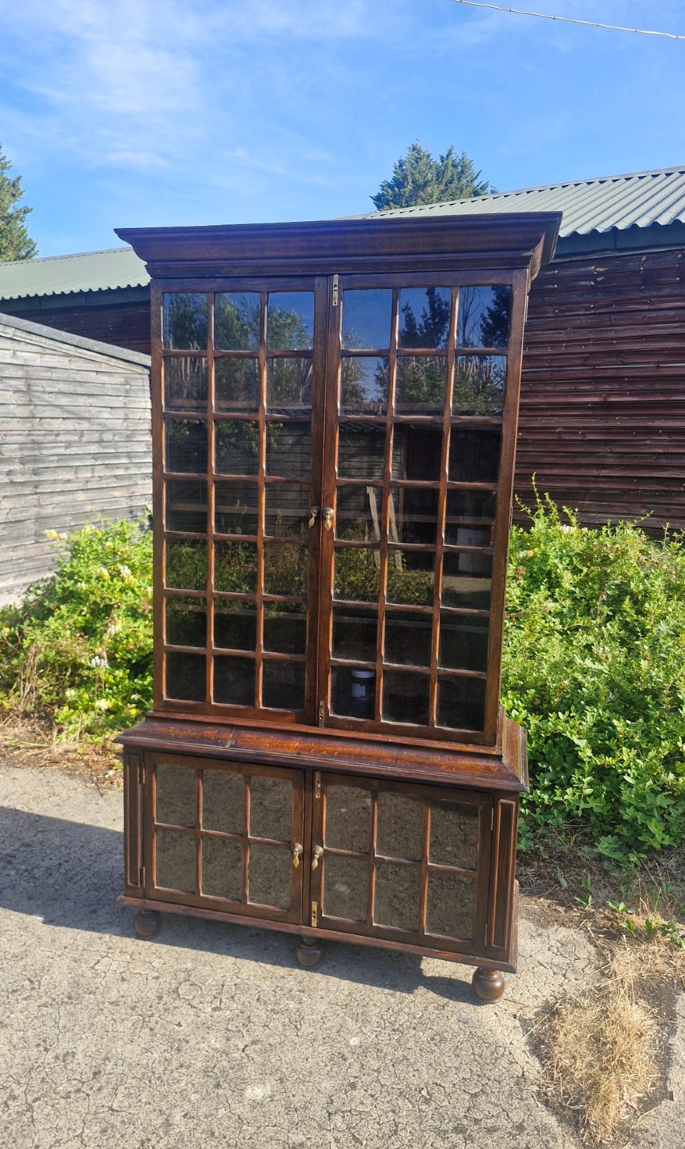 A two-part dark oak bookcase featuring upper and lower glazed double doors with multi-pane glass panels, standing on bun feet. View IV