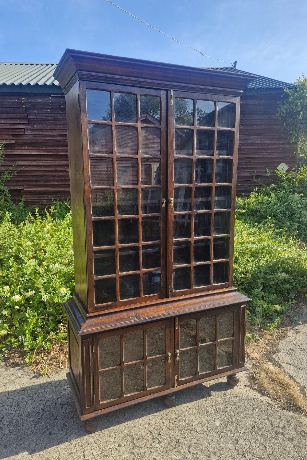 A two-part dark oak bookcase featuring upper and lower glazed double doors with multi-pane glass panels, standing on bun feet. View V