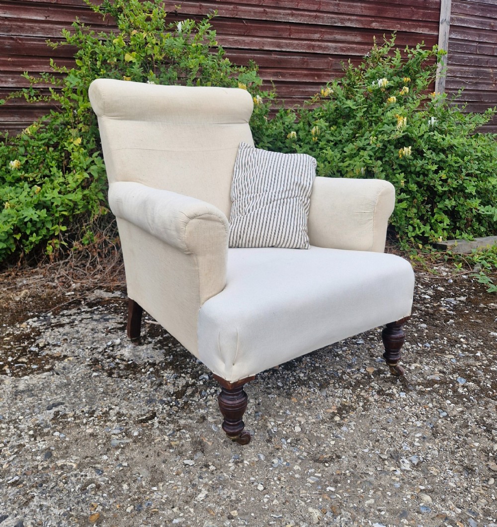 A late Victorian upholstered armchair in neutral cream fabric featuring a scrolled backrest, padded armrests, and turned mahogany front legs on brass castors.
